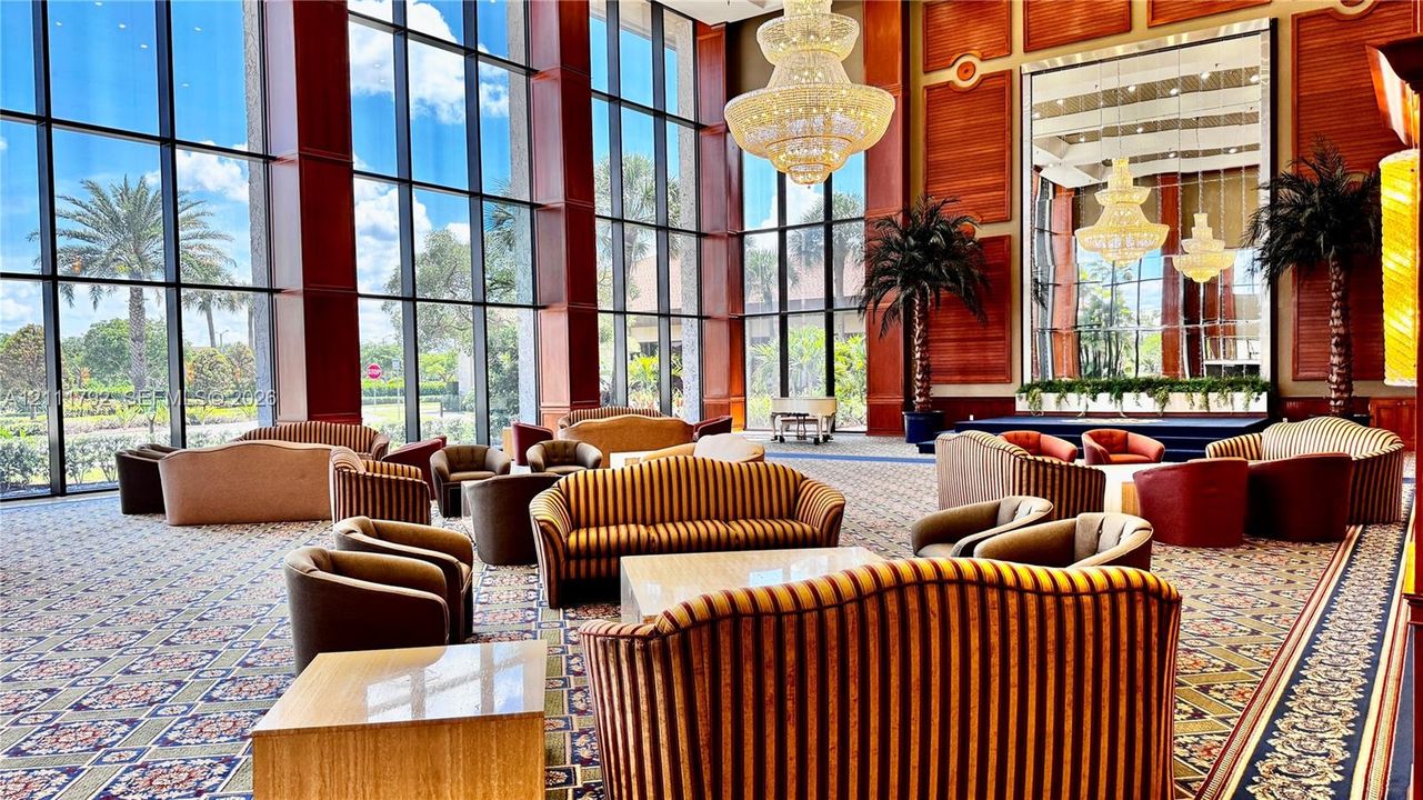 Grand atrium featuring floor-to-ceiling windows, soaring ceilings, polished wood-finish wall paneling, and an oversized crystal chandelier