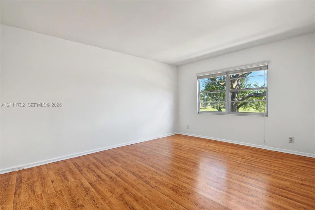 Interior space featuring wood-finish flooring, white walls, and a multi-pane window with blinds