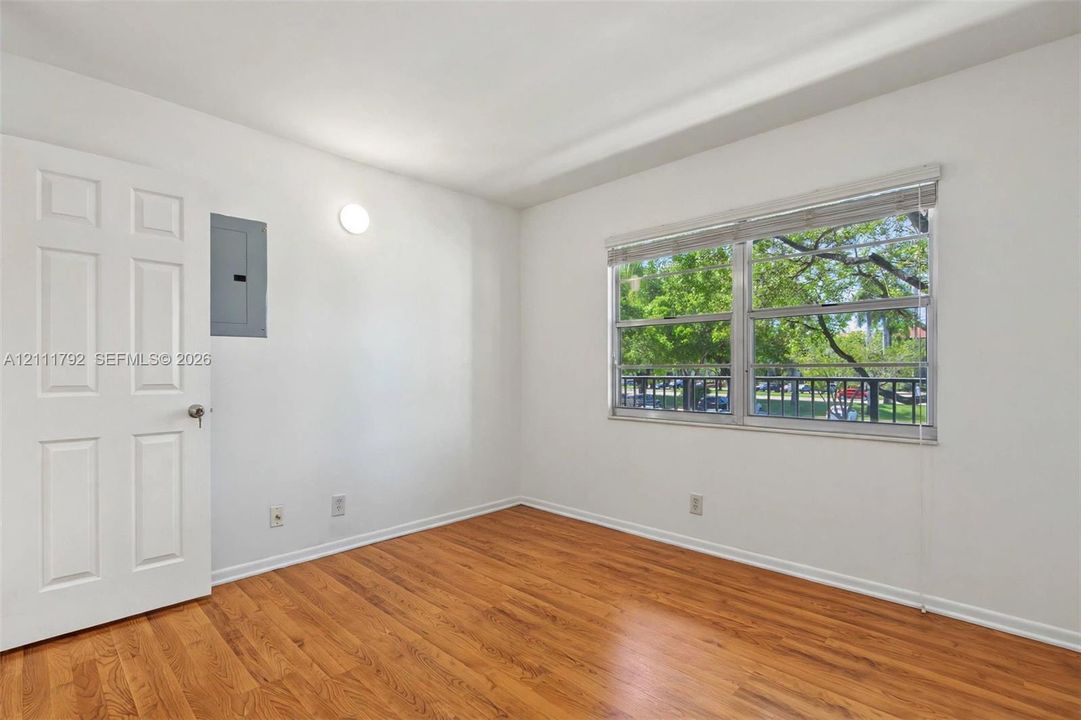 Room featuring wood-finish flooring, a two-panel interior door, and a horizontal sliding window with metallic blinds
