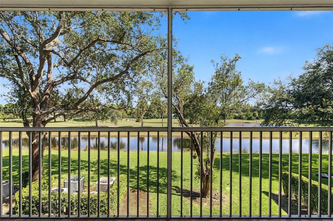 Screened-in balcony featuring metal railing, mature trees, landscaped grounds, and a water feature
