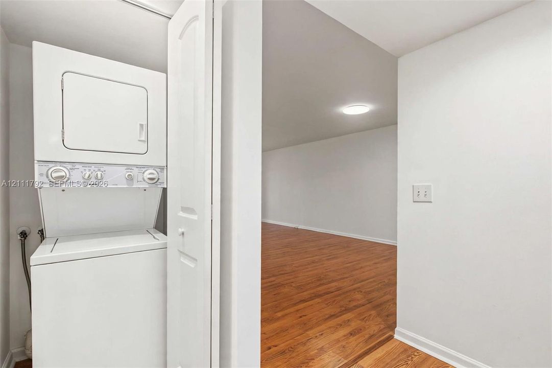 Stacked laundry unit with wood-finish flooring and flush-mount overhead lighting