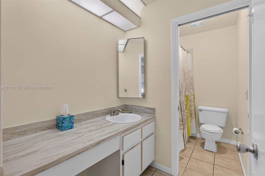 Bathroom vanity featuring a wood-patterned countertop, integrated basin with metal hardware, white cabinetry, a rectangular wall-mounted mirror, and ceramic tile flooring