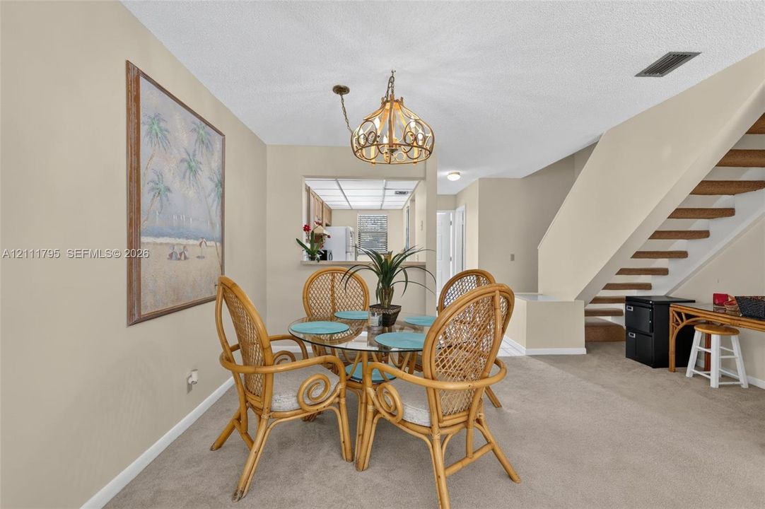 Neutral-toned dining area featuring a tiered metal chandelier, staircase with open-riser wood treads, and a pass-through window looking into the kitchen