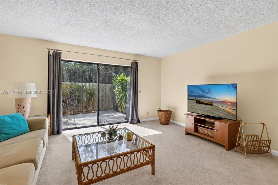 Living space featuring neutral carpeting, a textured ceiling, and large sliding glass doors providing outdoor access to a paved patio area