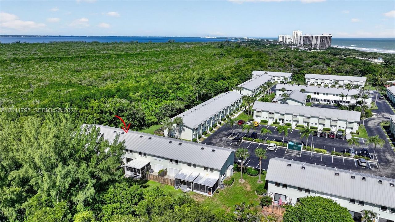 Aerial perspective of multi-unit property featuring metal roof structures, paved parking areas, and mature landscape surroundings with coastal proximity