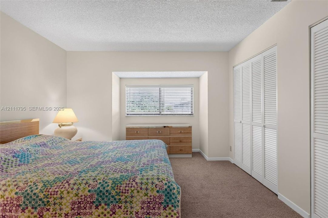Recessed window nook featuring a horizontal window with blinds, carpeted flooring, and floor-to-ceiling closets with louvered doors