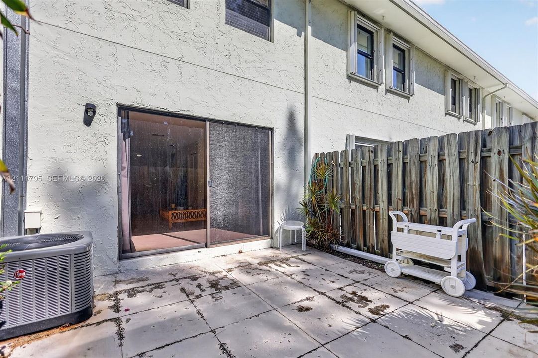 Rear exterior featuring a concrete paver patio, sliding glass door, and a wood privacy fence