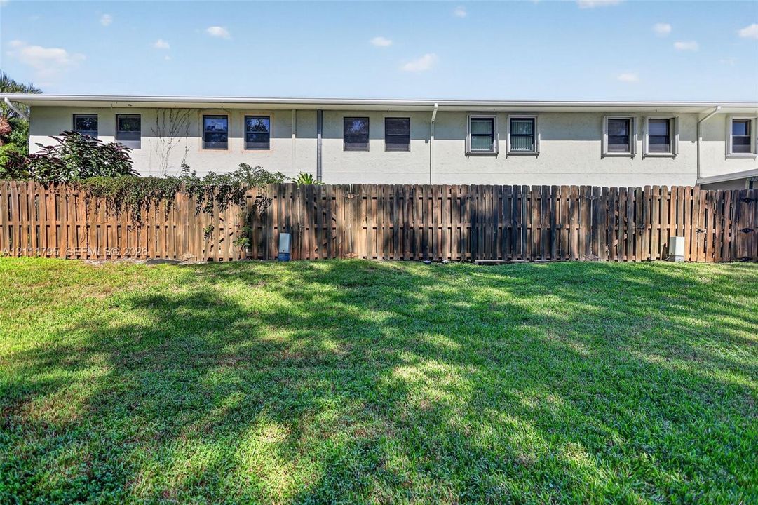 Expansive backyard featuring a manicured lawn, wood-slat privacy fencing, and a light-colored stucco exterior finish