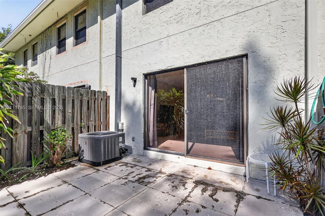 Concrete patio with sliding glass door access, enclosed by a wood privacy fence and finished with a stucco exterior