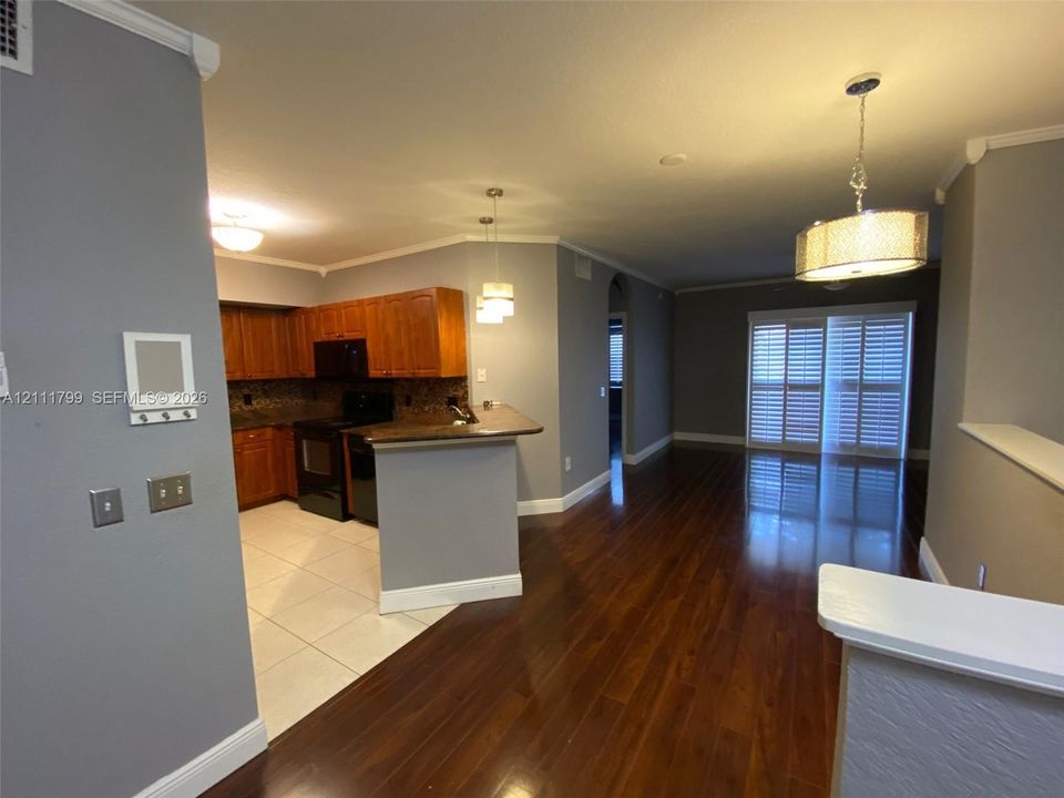 Kitchen featuring wood cabinetry, solid surface countertops, and tile flooring, paired with wood-finish flooring, crown molding, and sliding glass doors