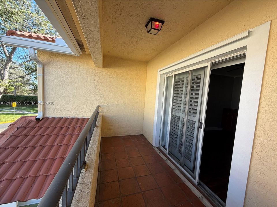 Covered balcony featuring terracotta-style tile flooring, metal railing, exterior lighting fixture, and sliding glass door