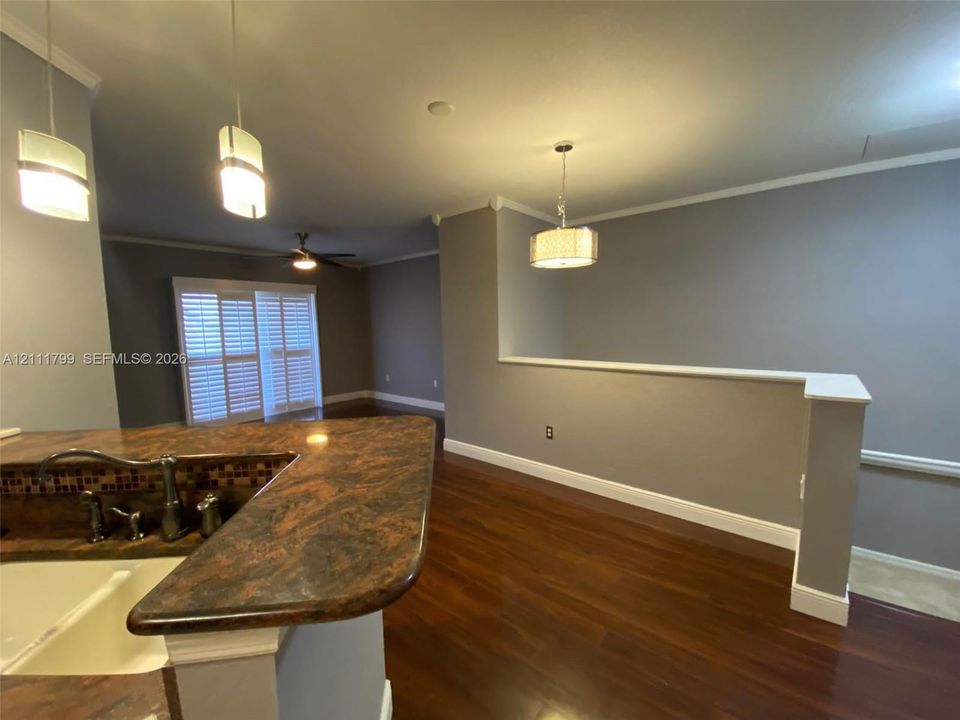 Kitchen featuring a stone-surface breakfast bar with a drop-in sink, wood-finish flooring, crown molding, tiered pendant lighting, and interior shutters
