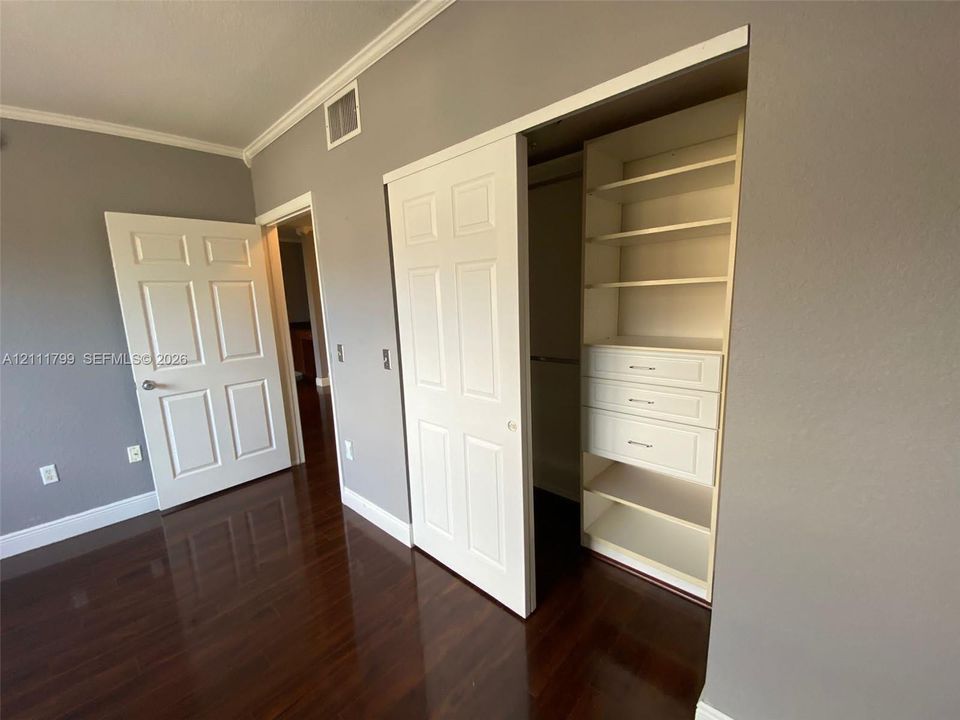 Dark-toned wood-finish flooring, white six-panel interior doors, and a custom built-in closet featuring adjustable shelving and integrated drawers