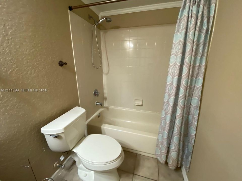 Full bathroom featuring a tub-shower combination with tiled surround, chrome fixtures, integrated soap dish, and neutral tile flooring