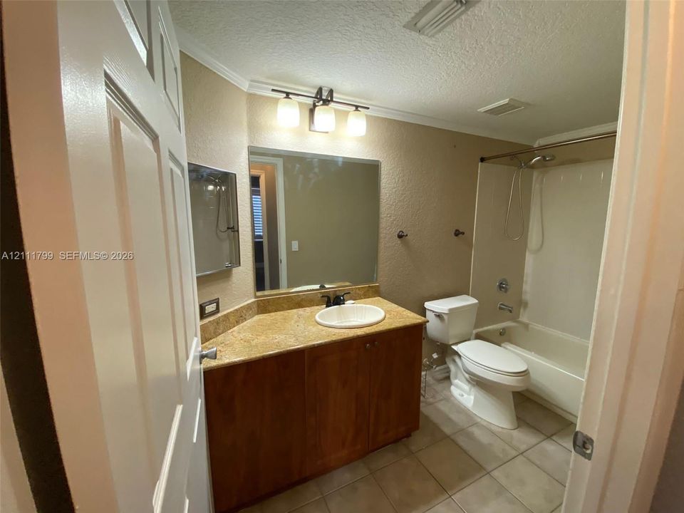 Bathroom featuring a wood-finish vanity with a stone-surface countertop, integrated circular basin, three-light wall fixture, and a tile-surround tub