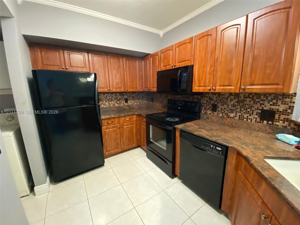 Kitchen featuring stained wood cabinetry, stone-finish countertops, multi-tonal tile backsplash, black built-in appliances, and tile flooring