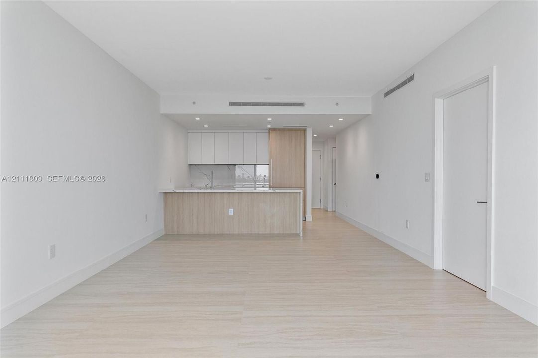 Open-concept interior featuring wood-finish flooring, recessed lighting, and a kitchen equipped with white cabinetry, light wood-toned base cabinetry, and a stone-surface island