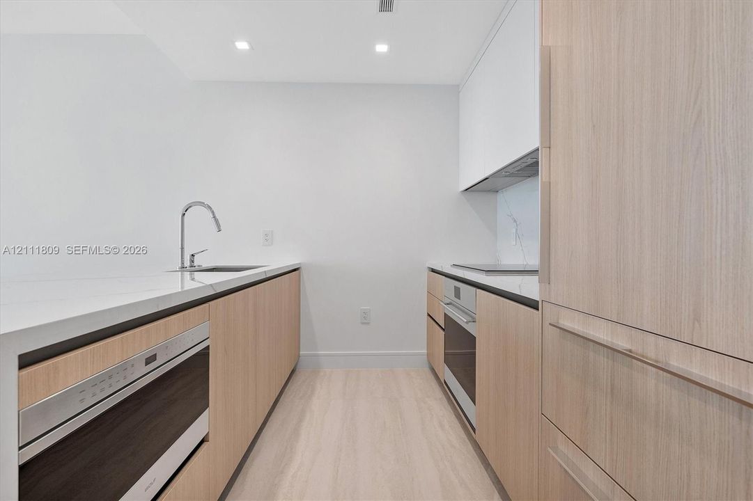 Kitchen featuring light wood-finish cabinetry, white stone countertops, recessed lighting, and integrated stainless steel appliances