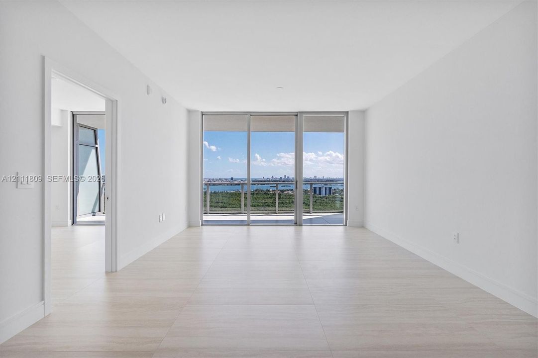 Open interior space featuring light-toned tile flooring, floor-to-ceiling glass sliding doors, and a metal-railed balcony