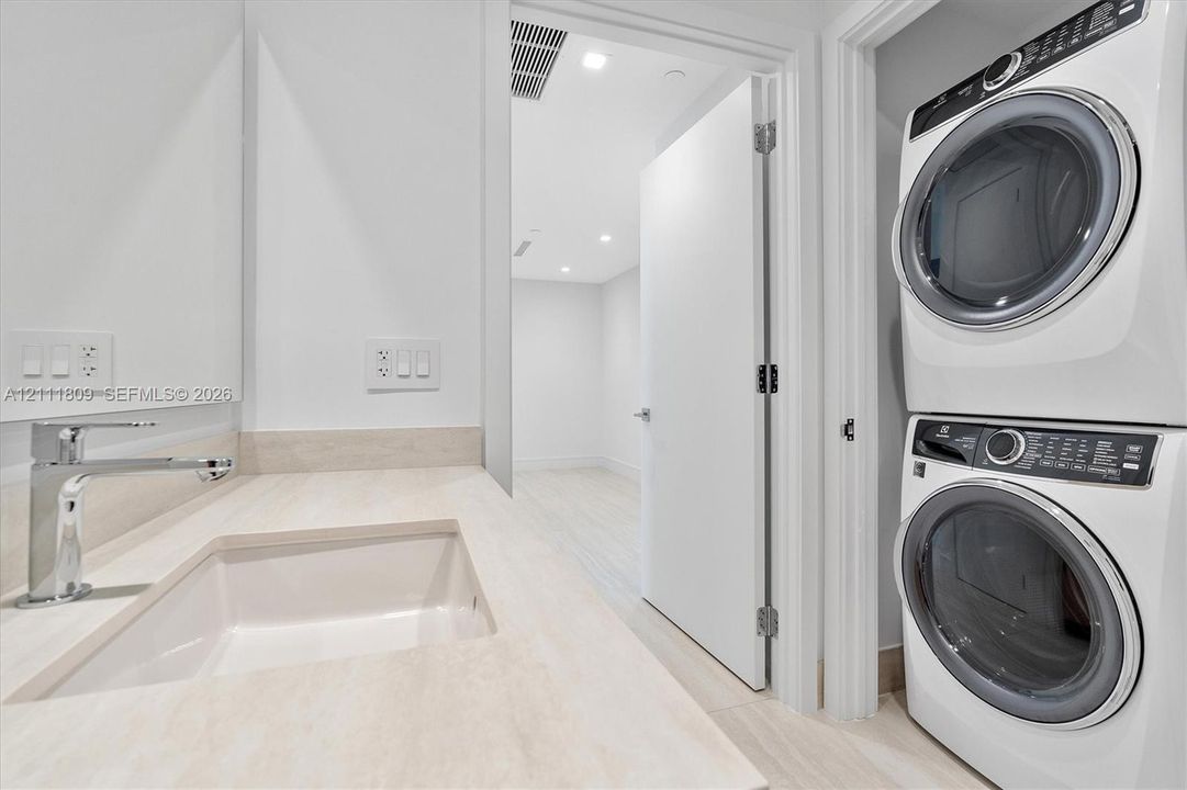 Integrated laundry area featuring a stacked washer and dryer, accompanied by a vanity with a stone countertop, recessed sink, and polished metal faucet