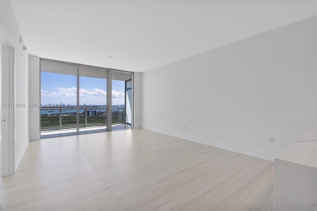 Open-concept room featuring floor-to-ceiling glass sliding doors, light-toned wood-finish flooring, and a glass-paneled balcony