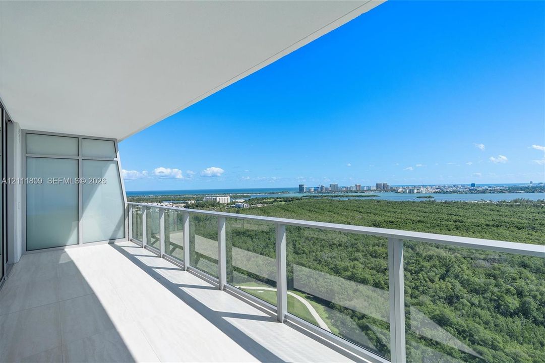 Covered balcony featuring large-format tile flooring, glass panel railings, and floor-to-ceiling windows