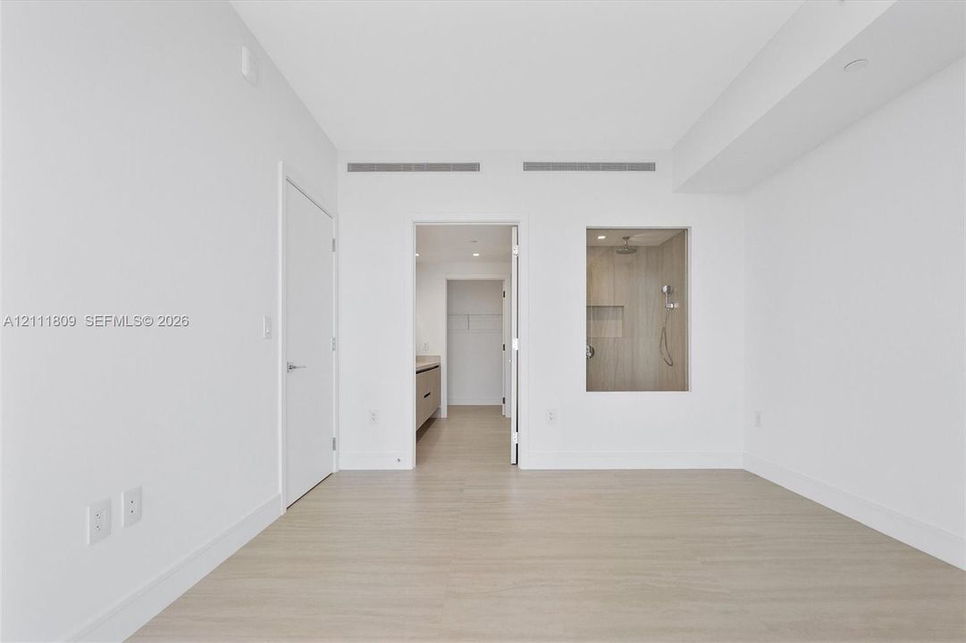Interior space featuring neutral wall tones, wood-finish flooring, and a glass-enclosed shower area with wall-mounted plumbing fixtures and a built-in recessed shelf