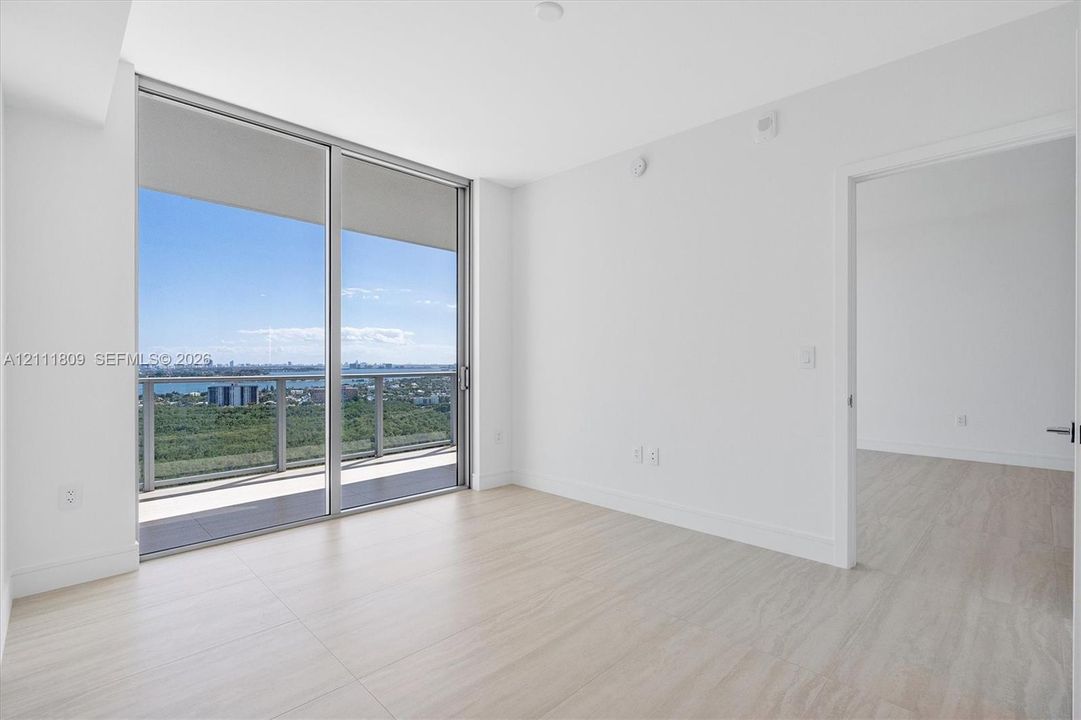 Floor-to-ceiling sliding glass door, private balcony with metal railing, and neutral wood-finish flooring