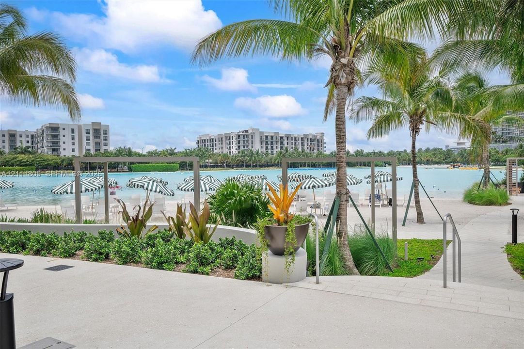 Expansive turquoise lagoon with a white sand shoreline, concrete patio, custom metal pergolas, and mature palm trees