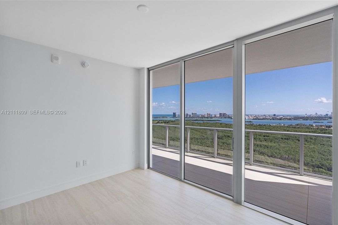 Floor-to-ceiling glass sliding doors, private balcony with metal railing, and neutral wood-finish flooring