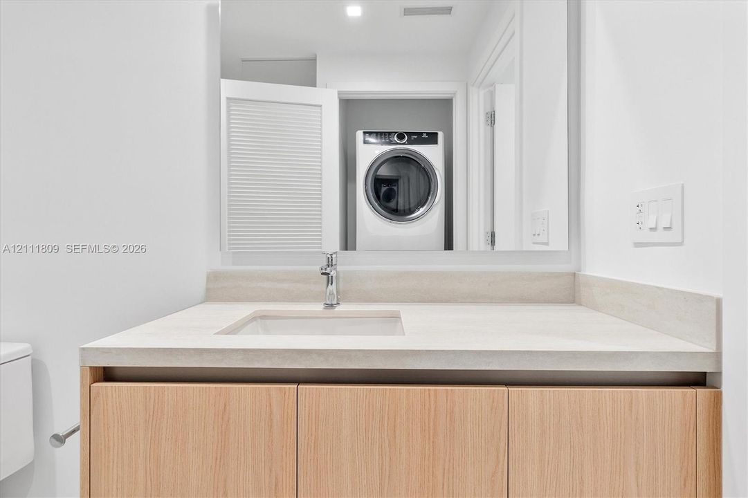 Bathroom vanity featuring a wood-finish cabinet, integrated countertop with a rectangular basin, and a wall-to-wall mirror