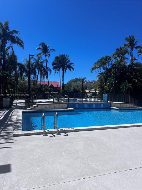 In-ground swimming pool with stone coping, metal safety fencing, concrete decking, and decorative tile accents