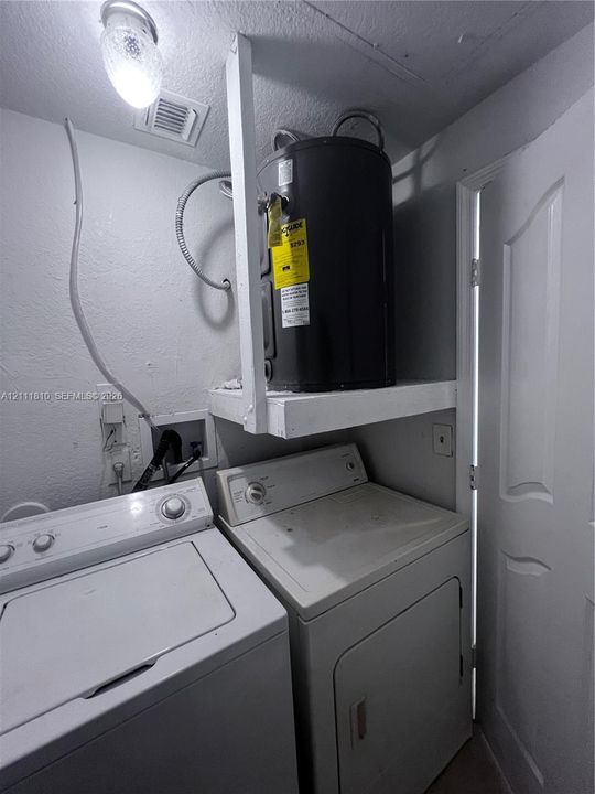 Dedicated utility area featuring an electric water heater mounted on a structural shelf, wall-mounted electrical outlets, and a flush-mount ceiling light fixture