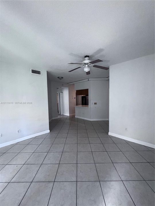 Neutral-toned interior space featuring large-format ceramic tile flooring, a central ceiling fan with integrated lighting, and an open-concept service counter with wood-finish cabinetry