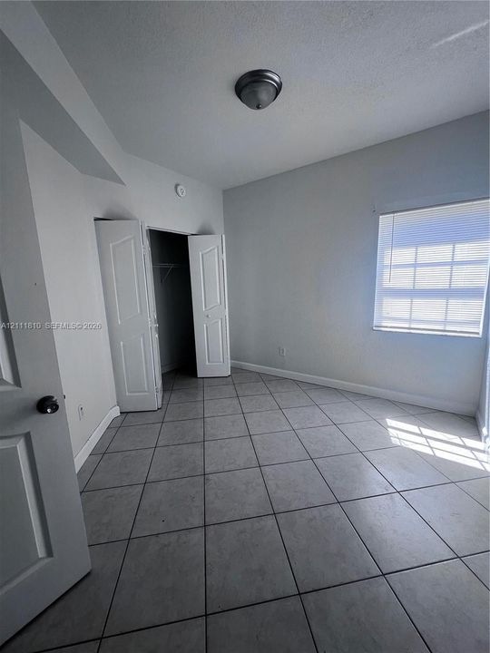 Large-format ceramic tile flooring, neutral wall tones, multi-panel closet doors, and window blinds
