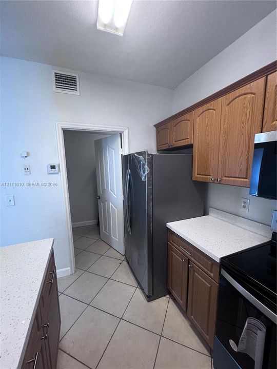 Kitchen featuring wood cabinetry, stone-finish countertops, tile flooring, and stainless steel refrigerator