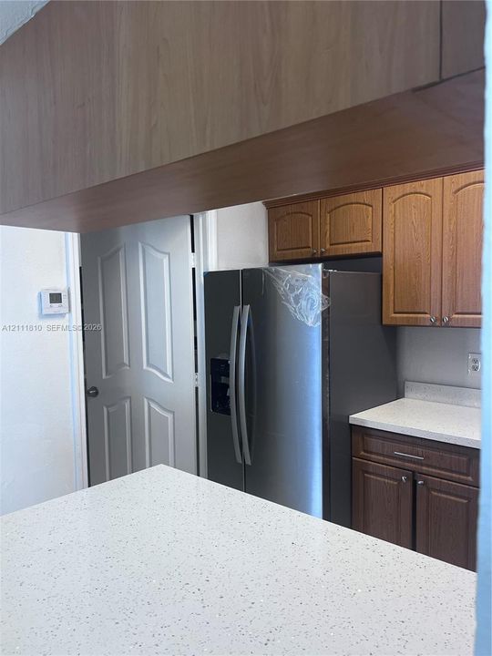 Kitchen featuring wood-tone cabinetry, stone-finish countertops, stainless steel side-by-side refrigerator, and arched-panel interior door