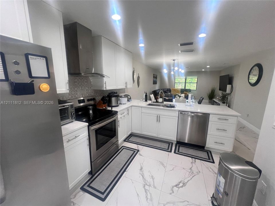 Kitchen featuring white shaker-style cabinetry, stainless steel appliances, a stone-finish countertop, patterned tile backsplash, and large-format porcelain tile flooring