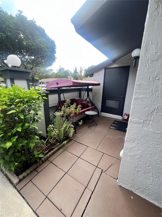 Exterior patio featuring large-format square tile flooring, textured stucco wall finish, and wall-mounted globe lighting fixtures