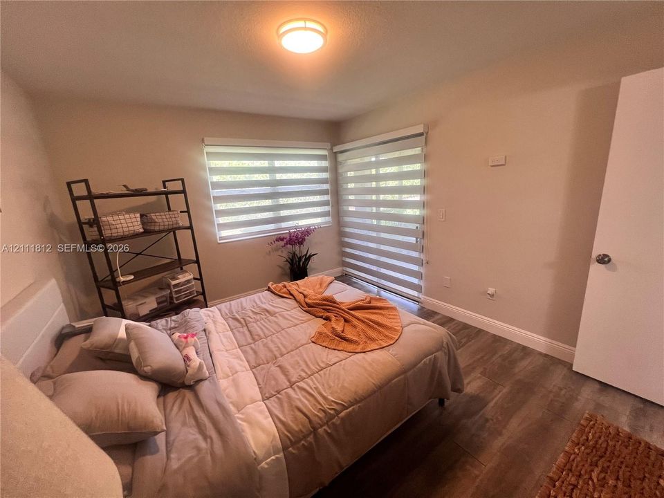 Interior space featuring wood-finish flooring, dual windows with installed light-filtering shades, and a sliding glass door