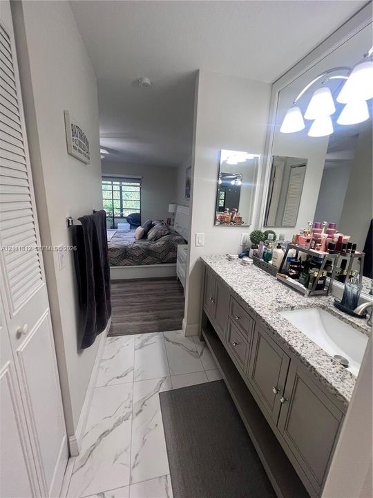 Vanity featuring stone-style countertop, undermount sink, multi-drawer cabinetry with bottom shelf, oversized mirror, and integrated multi-bulb lighting, complemented by large-format tile flooring