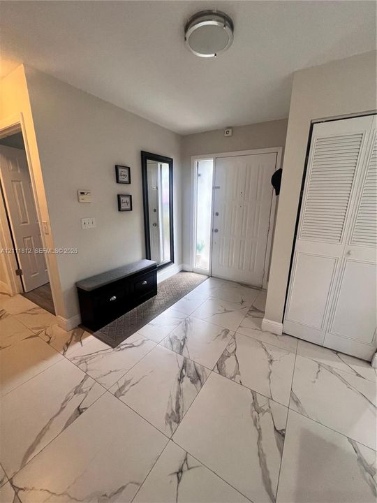 Entryway featuring large-format tile flooring with a veined pattern, a six-panel front door with an integrated glass sidelight, flush-mount ceiling lighting, and a closet with white louvered bifold doors