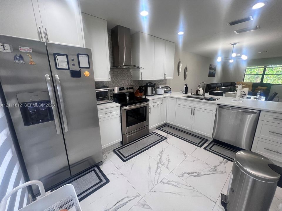 Kitchen featuring white cabinetry, stainless steel appliances, patterned tile backsplash, light-toned stone-finish tile flooring, and a peninsula countertop