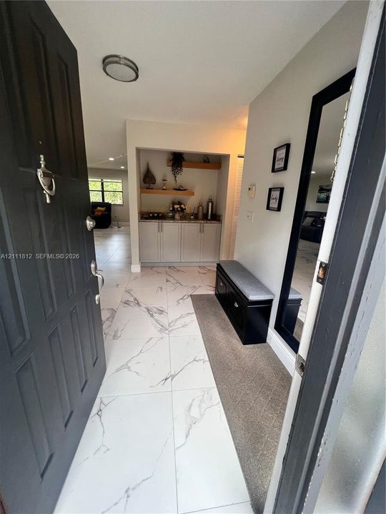 Entryway featuring large-format tile flooring, built-in cabinetry with natural wood shelving, and flush-mount ceiling lighting