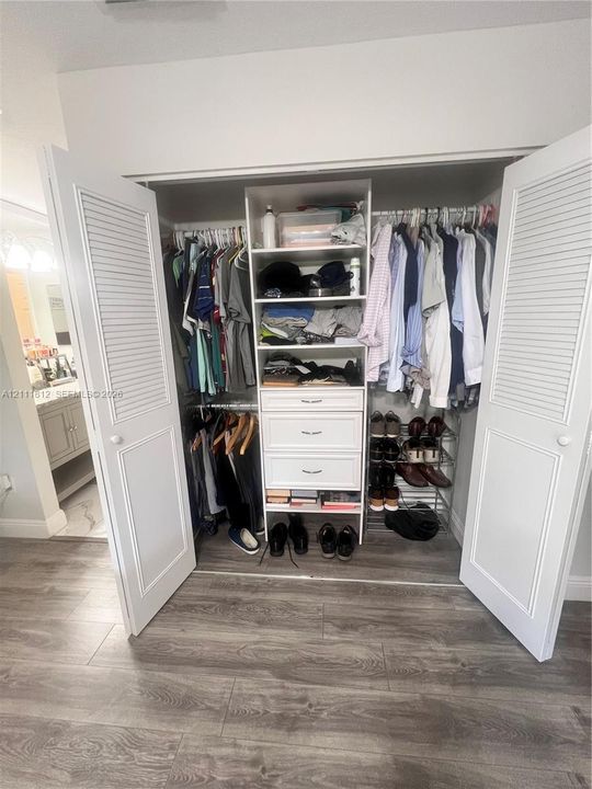 Reach-in closet featuring white louvered double doors, custom built-in white shelving, three integrated drawers, and wood-finish flooring