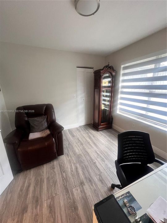 Room featuring wood-finish flooring, a bi-fold closet door, a flush-mount ceiling light fixture, and large windows with horizontal-band roller shades