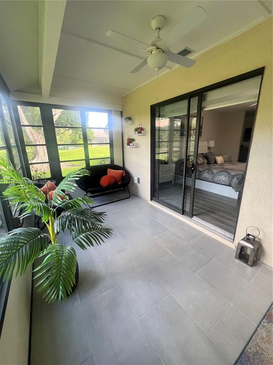 Screened-in porch featuring large-format ceramic tile flooring, a white ceiling fan, and sliding glass doors with dark frames