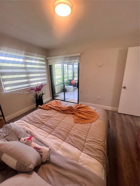 Room featuring wood-finish flooring, sliding glass door with roller shade, neutral wall paint, and overhead flush-mount lighting