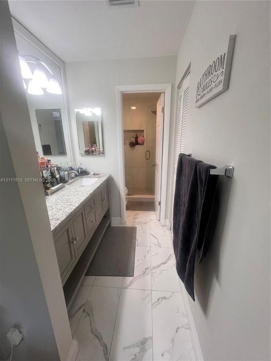 Bathroom vanity with stone-patterned countertop, under-mount sink, multi-drawer cabinetry, large wall-mounted mirror, and tile flooring with natural stone veining