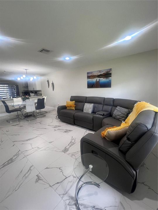 Large-format tile flooring with marble-style veining, recessed lighting, and modern multi-light chandelier